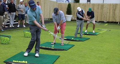 A photo of several golfers taking swings at a practice tee.