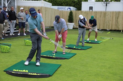 A photo of several golfers taking swings at a practice tee.