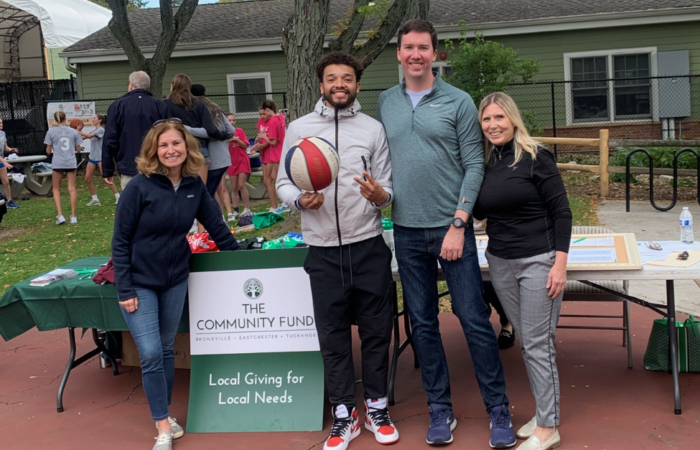 Four people of of different races and genders pose for a photo at an outdoor basketball tournament.