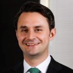 An image of a White man with brown hair wearing a green tie and a dark suit.