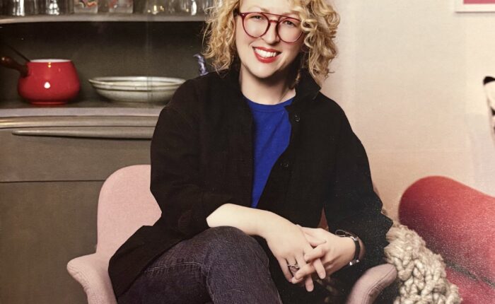 A photo of a magazine cover featuring a White woman with blonde hair who is seated in a pink chair in a home setting.