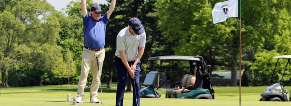 A golfer raises his hands above his head in victory while another golfer sinks a putt.