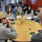 Groups of 8-10 teenagers sit at round tables in discussion groups.