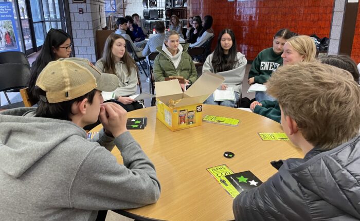 Groups of 8-10 teenagers sit at round tables in discussion groups.