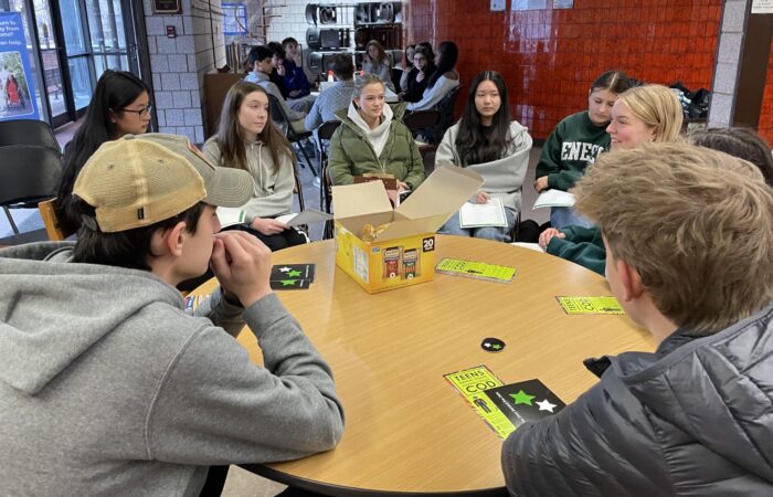 Groups of 8-10 teenagers sit at round tables in discussion groups.