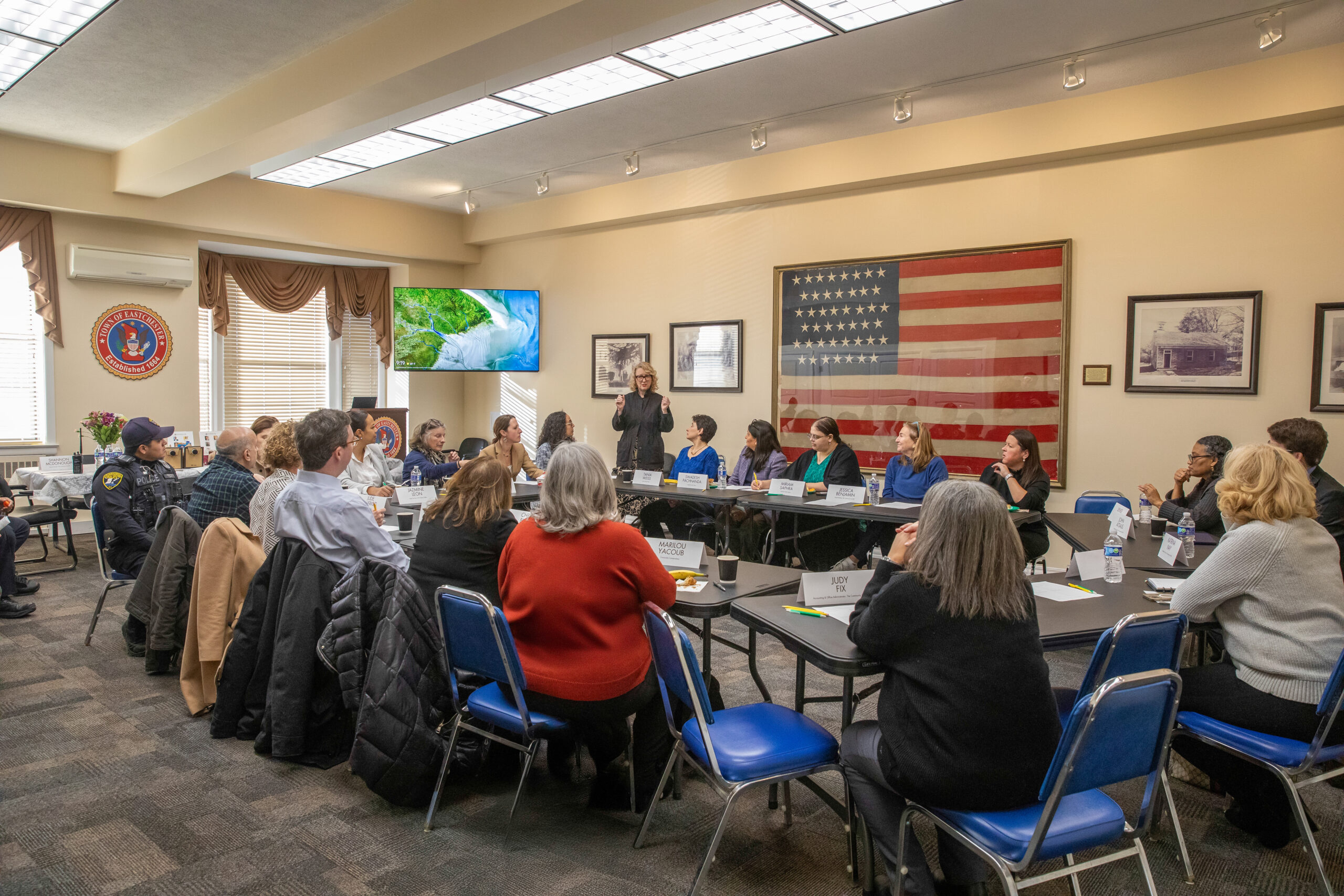 A group of 30 professionals and board members sit at a board room table during a conference.