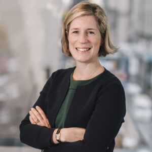 Photo of a White female with blonde hair wearing a green top and a black cardigan.