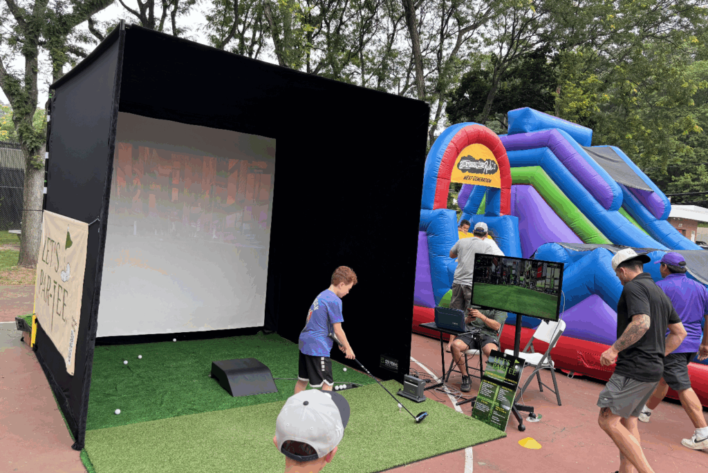 A student swings a golf club in a simulator at an outdoor community event.