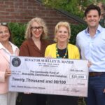 Photo of three women and one man posing for a photo, holding a facsimile of a check representing a grant.