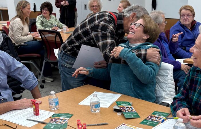 Photo of one older adult embracing another in a classroom setting.