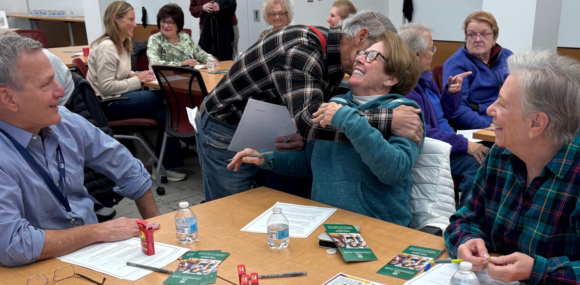 Photo of one older adult embracing another in a classroom setting.